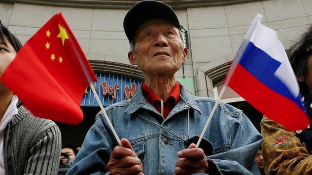 Elinde Rusya ve Çin bayrakları olan bir Çinli erkek