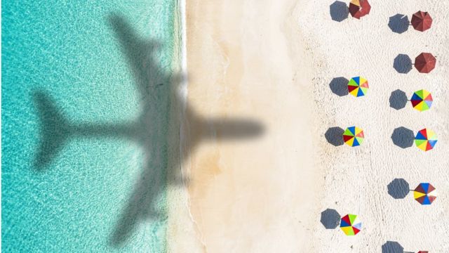 Sombra de avión sobre playa con parasoles en una isla del Caribe.
