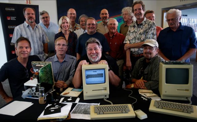 Funcionários antigos da Apple sorrindo para foto perto de computadores antigos