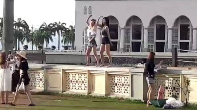 Dua perempuan tampak menari-nari di pagar masjid