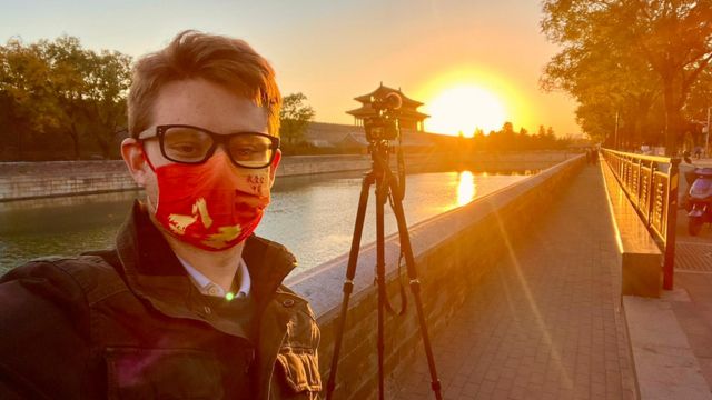 Ed Lawrence wearing a mask in front of his camera on a tripod next to a river