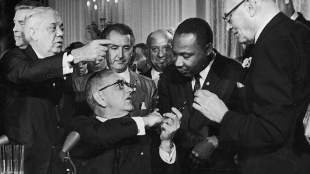 Черно-белое фото: Линдон Б. Джонсон пожимает руку доктору Мартину Лютеру Кингу во время подписания Закона о гражданских правах в Белом Доме в Вашингтоне