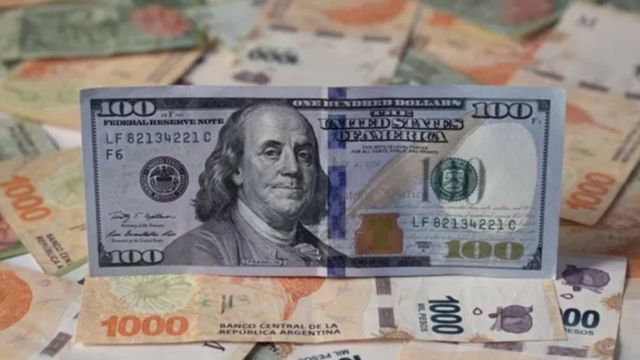 Un billete de 100 dólares sobre billetes de pesos argentinos