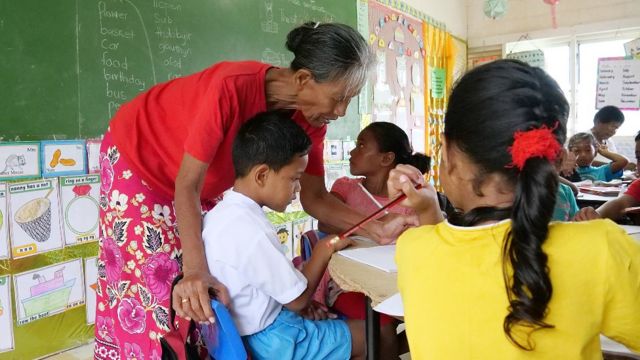 Professor corrigindo o trabalho de uma criança em uma escola em Tuvalu