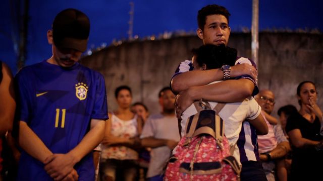 Estudantes e adultos se abraçam e olham consternados para entorno da escola Raul Brasil