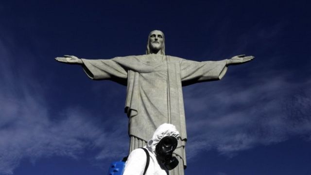 Homem todo coberto de trajes higiênicos em frente à estátua do Cristo Redentor