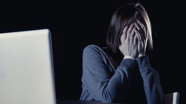 Mujer cubriéndose la cara frente a una computadora
