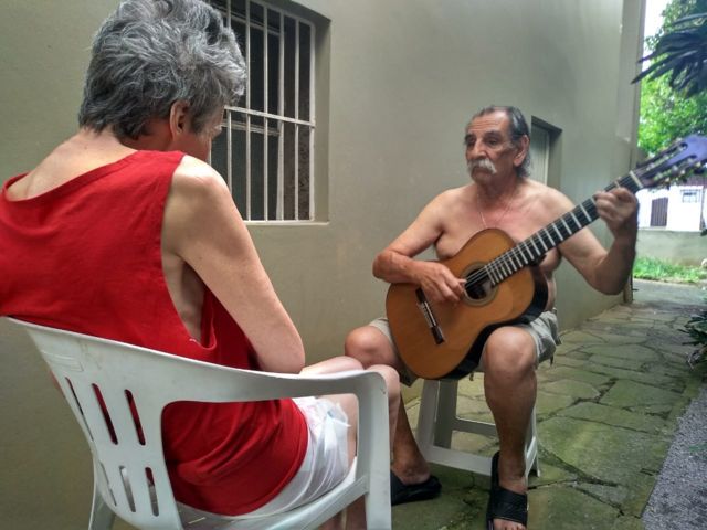 Imagem mostra o músico Lúcio Yanel tocando violão para a mulher, Sueli, que tem Alzheimer