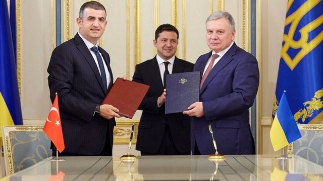 Халук Байрактар (слева) и министр обороны Украины Андрей Таран (справа) в присутствии президента Владимира Зеленского подписывают договор о сотрудничестве