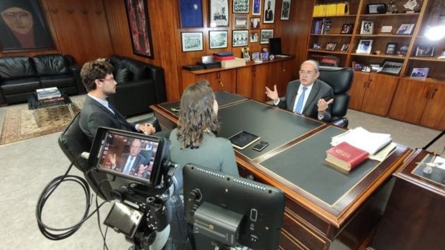 Em seu gabinete, Gilmar Mendes conversa com dois repórteres da BBC, todos filmados por câmera