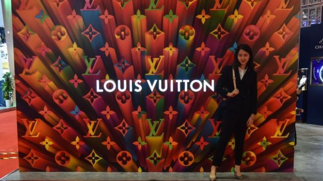 Una mujer china posa frente a un cartel publicitario de Louis Vuitton