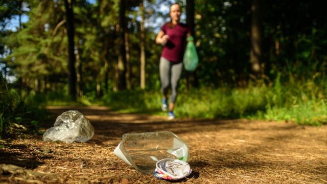 Mujer corriendo y recogiendo basura en un camino en un bosque