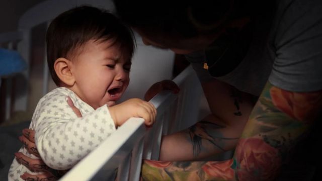 Mulher com braços tatuados atendendo ao choro de um bebê em seu berço