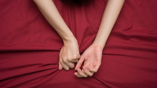 Brazos de una mujer sobre sábanas rojas.