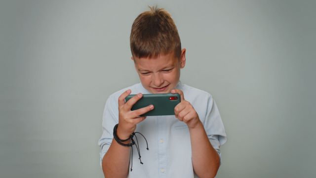Menino branco chorando ao olhar um celular