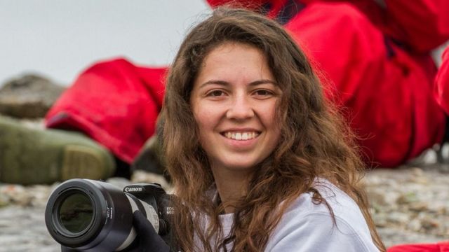 Danielle Waldman sorrindo para a câmera e segurando uma máquina fotográfica