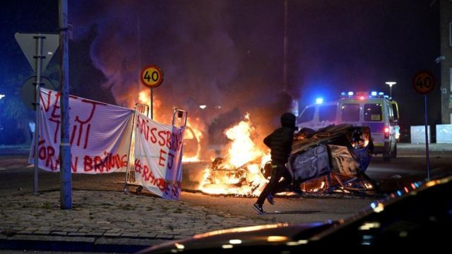 شخص يركض بينما تحترق السيارات أثناء أعمال الشغب في مالمو