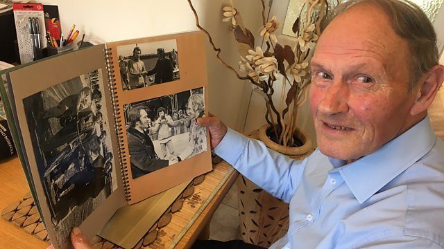 Edwin Overland with short dark hair wearing a blue shirt and looking through a photo album