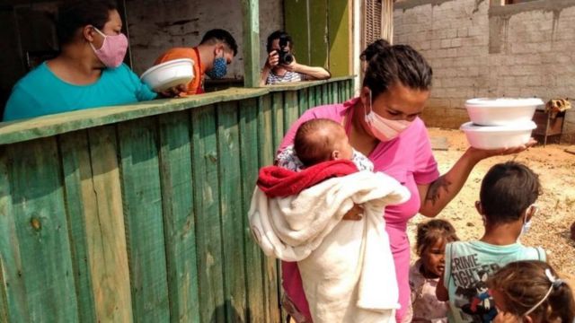 Mulher com filhos recebendo marmita durante a pandemia de covid-19