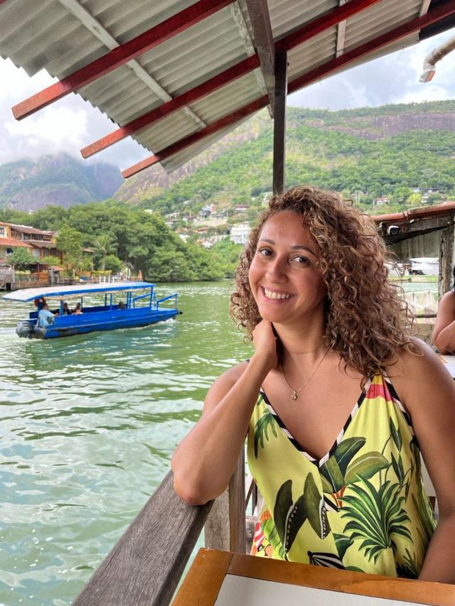A consultora brasileira residente em Portugal Renata Lima. Ela está  usando uma blusa amarela e sentada em uma varanda à beira de um rio