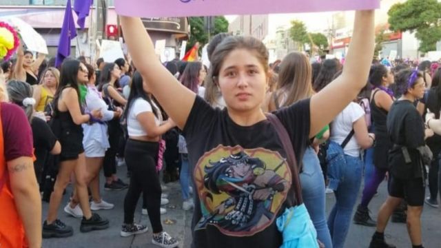 Mulher jovem usa blusa com desenho que faz alusão a Janequeo e segura um cartaz em protesto