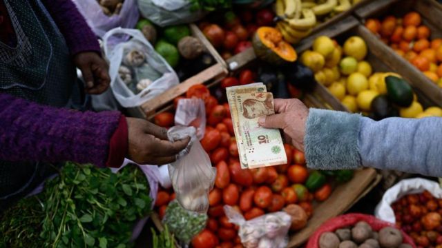 Una persona pagando con pesos argentinos en un mercado de frutas y verduras.