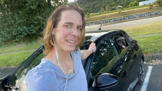 Indie Grant, a young white man with blond hair on his shoulder next to his car