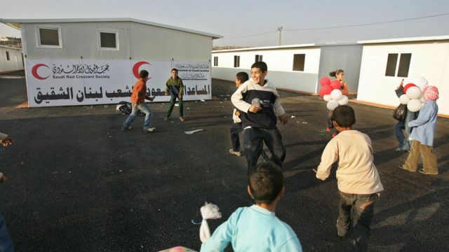 أطفال لبنانيون يلعبون وفي الخلفية لافتة حول الدعم السعودي للبنان