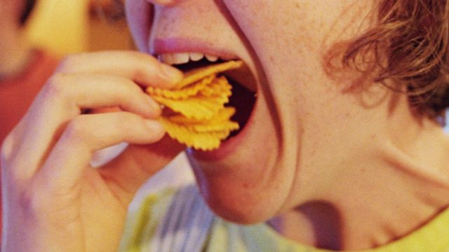 Una joven llenándose la boca de papas fritas