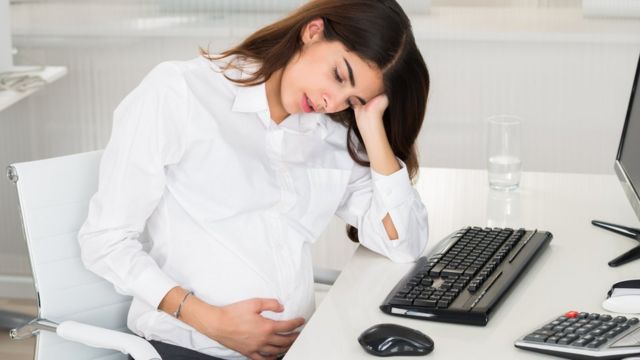 Mujer embarazada y cansada frente a una computadora.