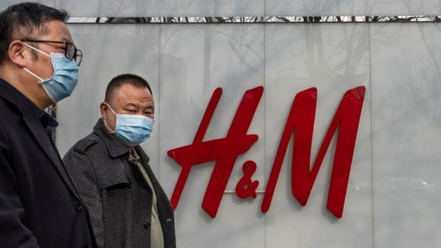 Dos hombre caminan frente a un logo en H&M en Shangái.