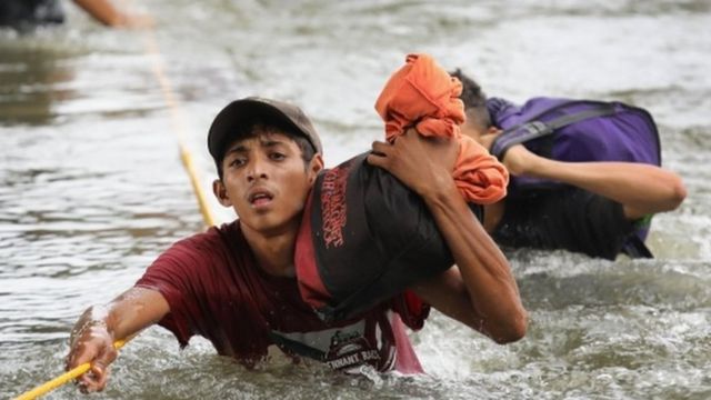 Migrantes caminan por el río para cruzar a México.