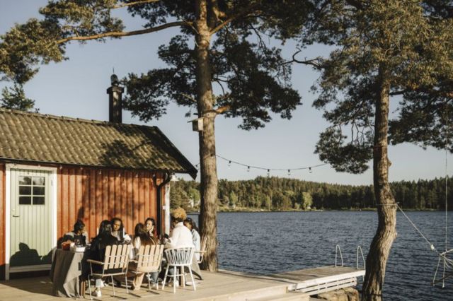 Pessoas reunidas ao redor de uma mesa do lado de fora de uma casa à beira de um lago