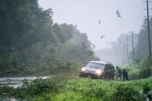 La gente trabaja para liberar un vehículo atrapado en el arcén entre ramas de árboles caídas por la tormenta cerca de Mayo, Florida.
