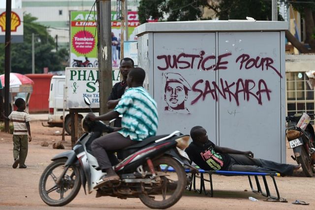People stand next to graffiti that reads "justice for Sankara".