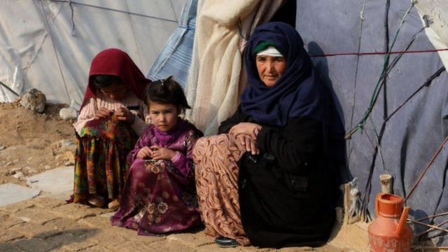 عائلة أفغانية تجلس أمام خيمة في ظروف صعبة.