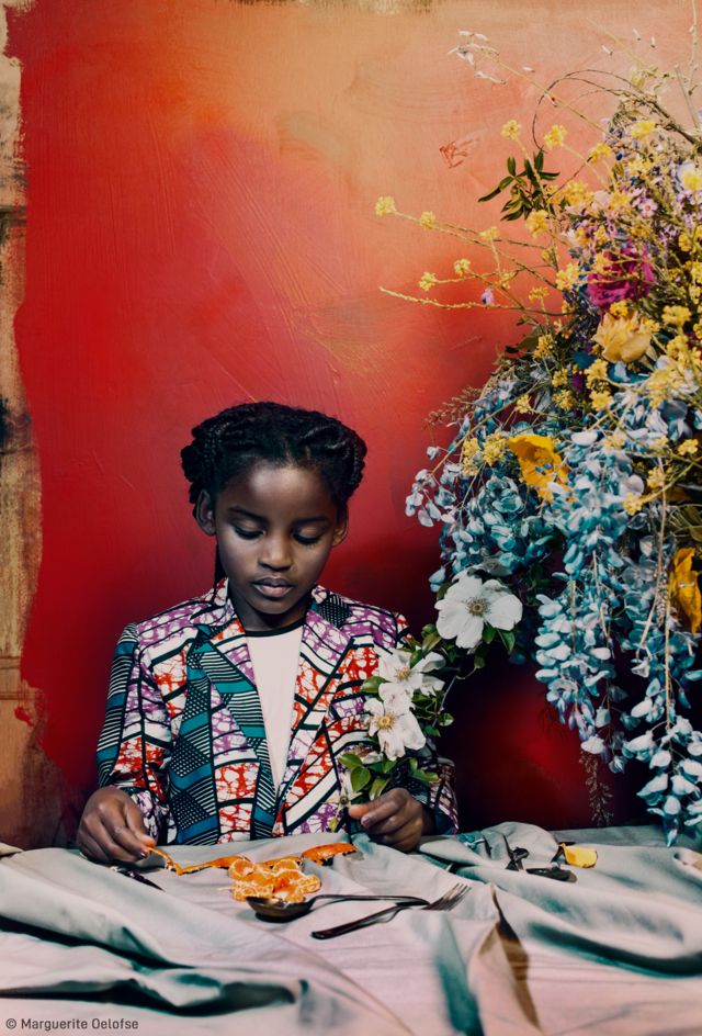 Una niña pelando fruta en una mesa, junto a un ramo de flores.