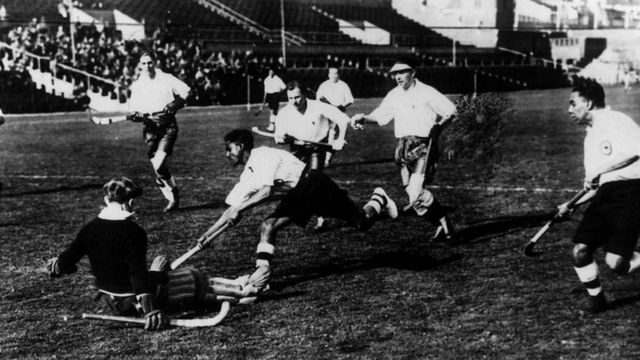 1928ની એમ્સ્ટર્ડમ ઑલિમ્પિક્સમાં એક હોકી મેચમાં પોતાનું કૌશલ્ય દેખાડી રહેલા ભારતીય ખેલાડી મેજર ધ્યાનચંદ.