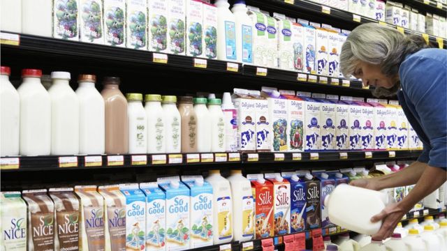Mulher escolhendo leite para comprar em prateleira de supermercado