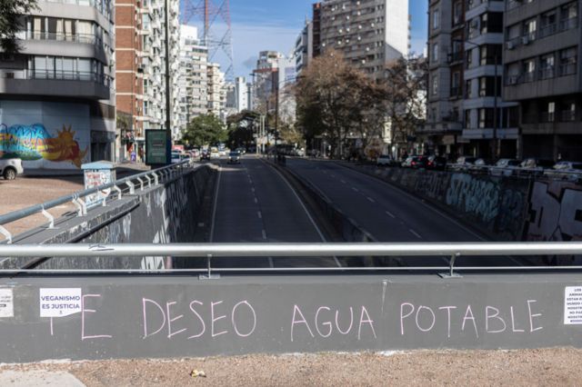 Un grafiti con la leyenda "Te deseo agua potable" sobre un pasaje encima de un túnel en una transitada avenida de Montevideo.