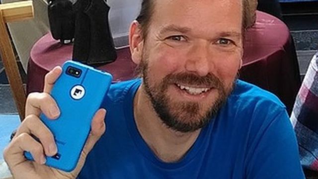 Urs Lesse um homem branco de barba castanha, segura um celular