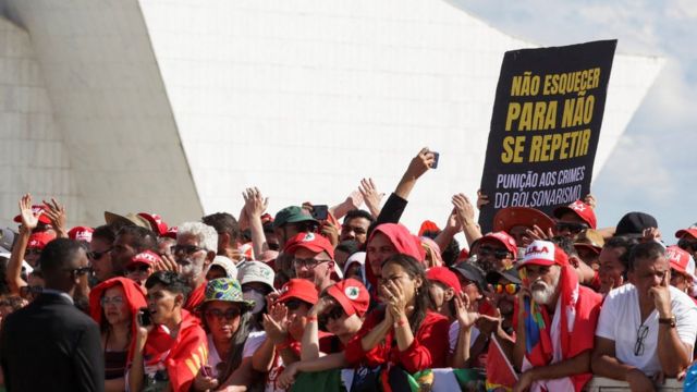 Dezenas de apoiadores em área externa de Brasília, com cartaz dizendo: "Não esquecer para não se repetir. Punição aos crimes do bolsonarismo"