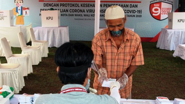 Ketua Kelompok Penyelenggara Pemungutan Suara (KPPS) memberikan surat suara kepada pemilih saat dilaksanakan Simulasi Pemungutan Suara dengan Protokol Kesehatan Pencegahan dan Pengendalian COVID-19 pada Pilkada Serentak 2020, di TPS 18 Cilenggang, Serpong, Tangerang Selatan, Banten, Sabtu (12/9/2020).