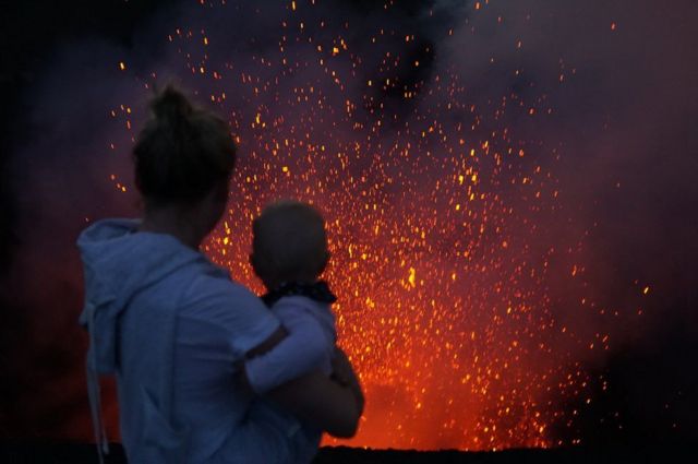 امرأ تحمل طفلة أمام بركان