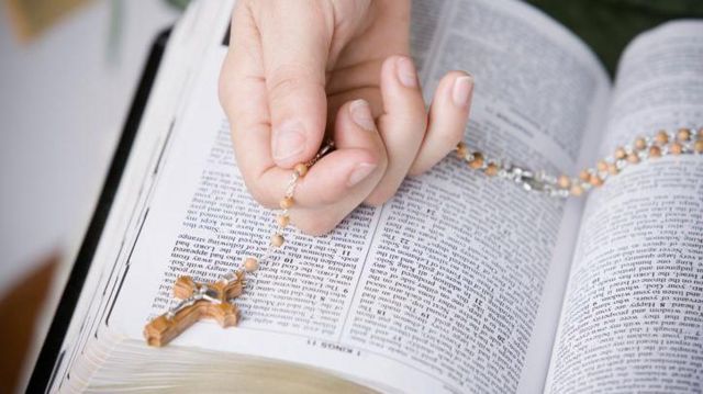 Pessoa segurando um terço em cima de uma Bíblia