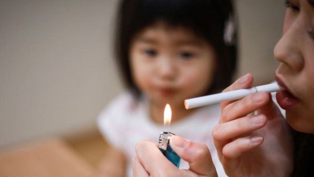 Une femme allume une cigarette devant un enfant