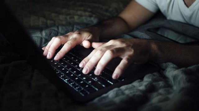 Mãos no teclado, em ambiente escuro, aparentemente um quarto