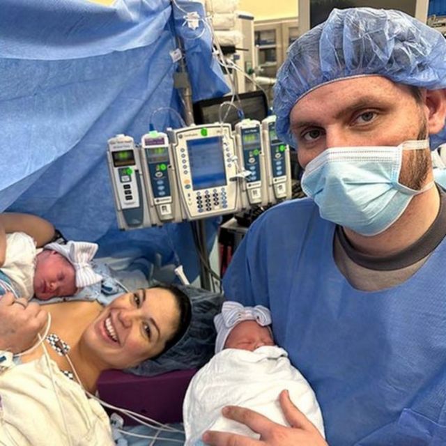Homem e mulher seguram bebês em sala de cirurgia