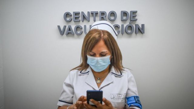 Profissional em centro de vacinação olha no celular