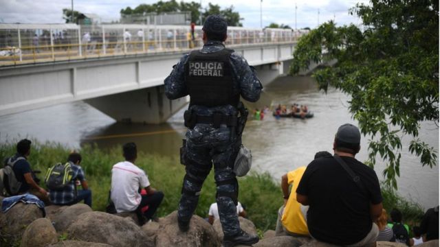 Un policía observa a migrantes en el río